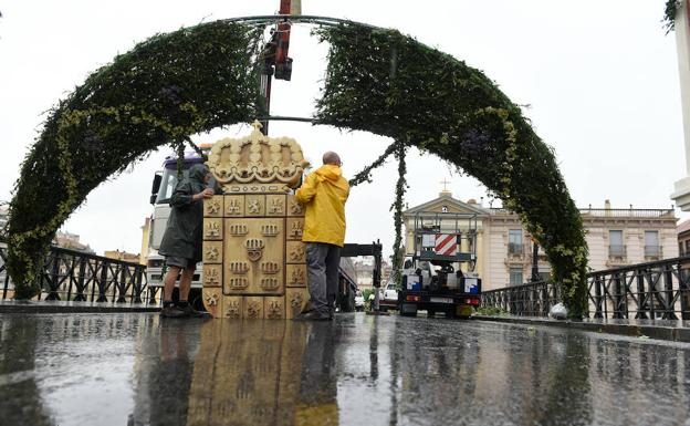 Operarios del Ayuntamiento levantan el arco floral instalado en el Puente Viejo de Murcia.