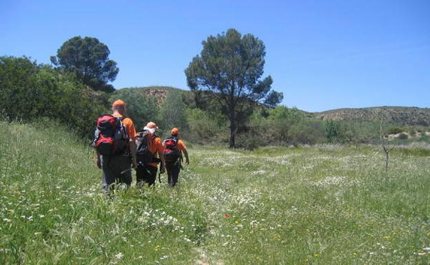 Tres senderistas caminan por un prado florido, a la salida de la Senda de la Huertecica y en dirección al río./