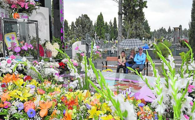 Una tumba, cuajada de ramos de flores de todos los colores. Al fondo, una familia medita sentada en un banco y se ampara bajo un mismo paraguas de la lluvia que cayó a primeras horas de la mañana de ayer./Guillermo Carrión / AGM