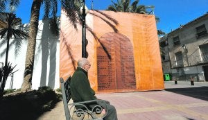 Un vecino, sentado en un banco, ante la portada simulada que da entrada a la carpa. :: PACO ALONSO / AGM/