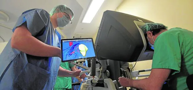 Ricardo Robles directs the movements of the Da Vinci robot from the console, while Miguel Ángel Navarro, from Cella Medical Solutions, checks the screen on which the three-dimensional image of the area affected by the tumor is displayed. 