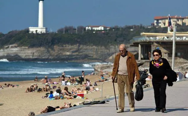 Two retirees walk in front of a beach. 