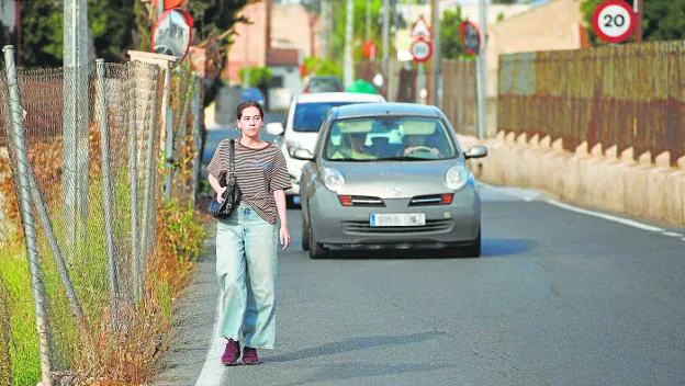 A young woman walks along the Senda de Granada in front of several vehicles, with which she shares the road and which must avoid her due to the absence of sidewalks. 