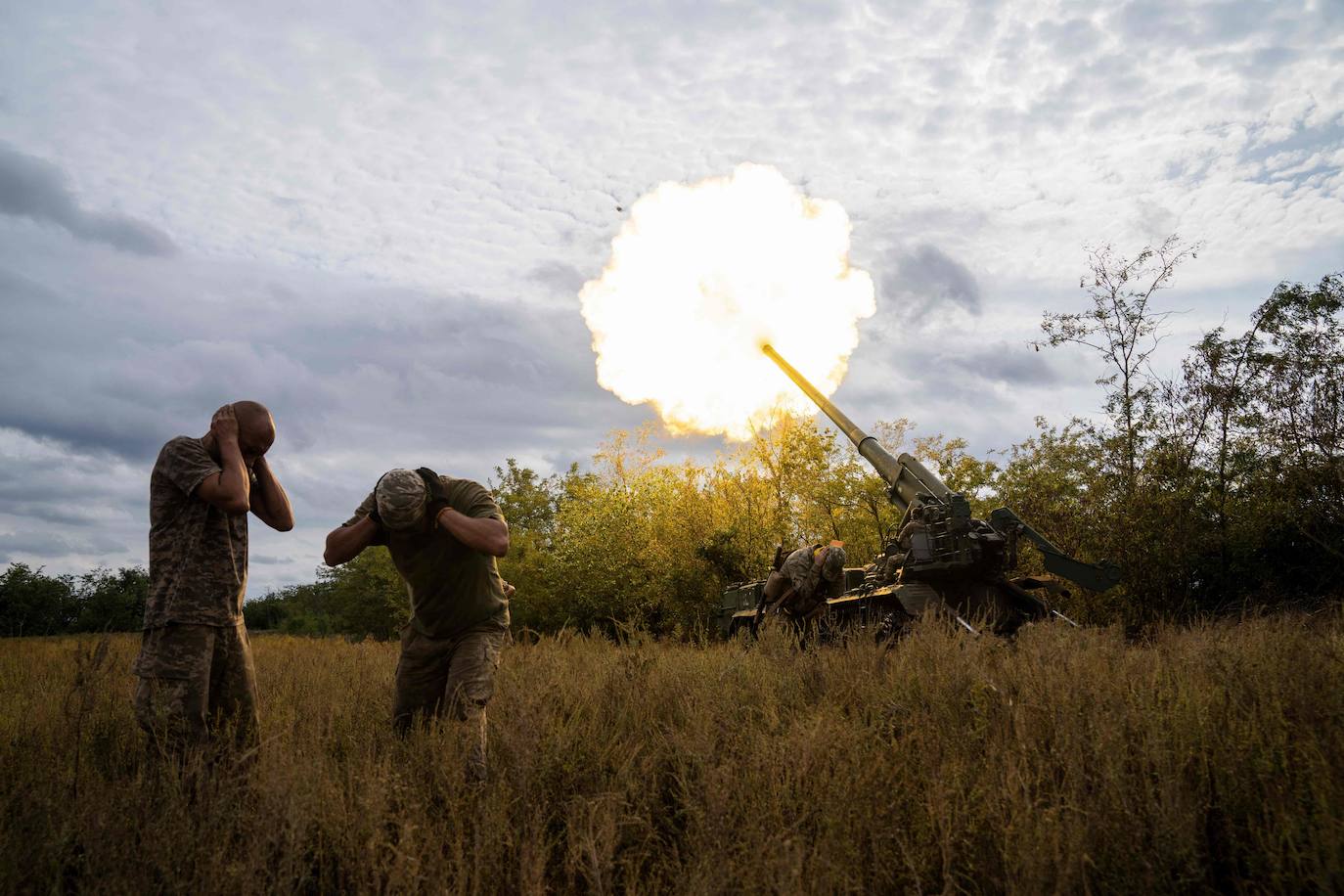 Two Ukrainian soldiers cover their ears as their artillery fires at Russian positions. 