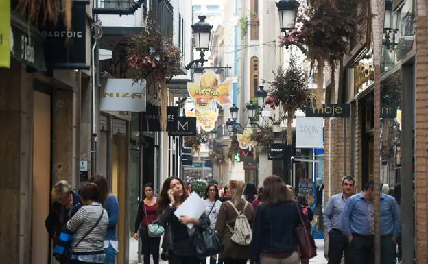 Pedestrians walk without shelter through a central street in Murcia during autumn. 