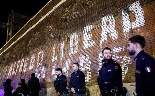 Italian policemen stand guard next to a wall on which there is a graffiti in favor of the release of anarchist Alfredo Cospito.